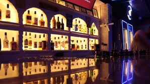 A bar area with multiple shelves of bottles, a reflective floor, and a neon sign in the background. - Taner Otel (Fethiye)