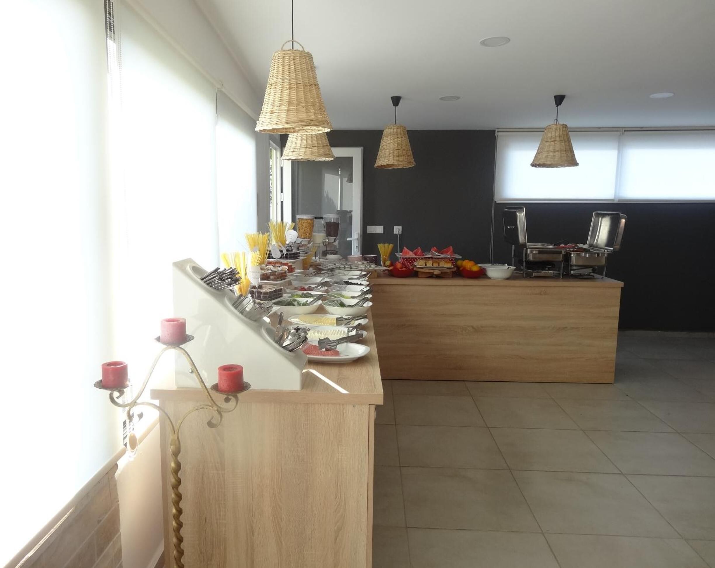Disposição de buffet com diversos alimentos e utensílios, balcão de madeira e luminárias de vime penduradas.