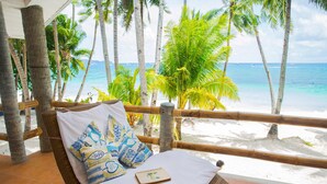 A wicker lounge chair with a white cushion and patterned pillows, overlooking a beach with palm trees and the ocean. - Mabuhay Beach House (Boracay Island)