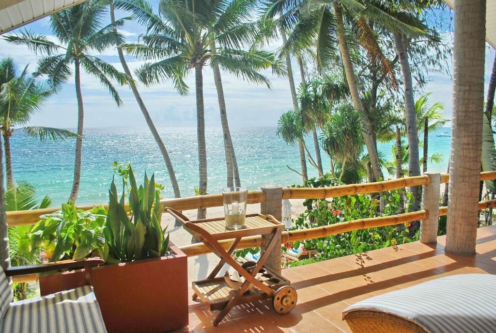 A balcony with a view of the ocean, palm trees, and a wooden cart with a glass and candle.