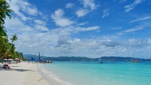 A beach with clear turquoise water, palm trees, and boats. - Mabuhay Beach House (Boracay Island)