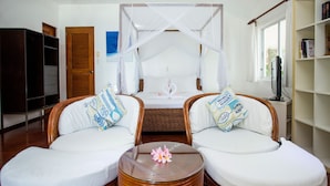 A bedroom with a canopy bed, two wicker chairs with cushions, a glass table with a flower, a wardrobe, and a bookshelf. - Mabuhay Beach House (Boracay Island)
