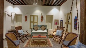 A cozy living room with wicker chairs, a sofa with patterned cushions, and a wooden coffee table. - French Haveli (Ahmedabad)