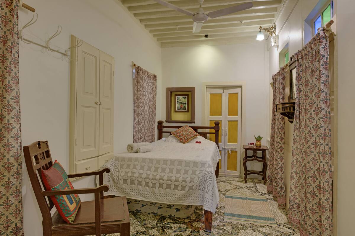 A bedroom with a bed, a chair, a small table, and a ceiling fan.