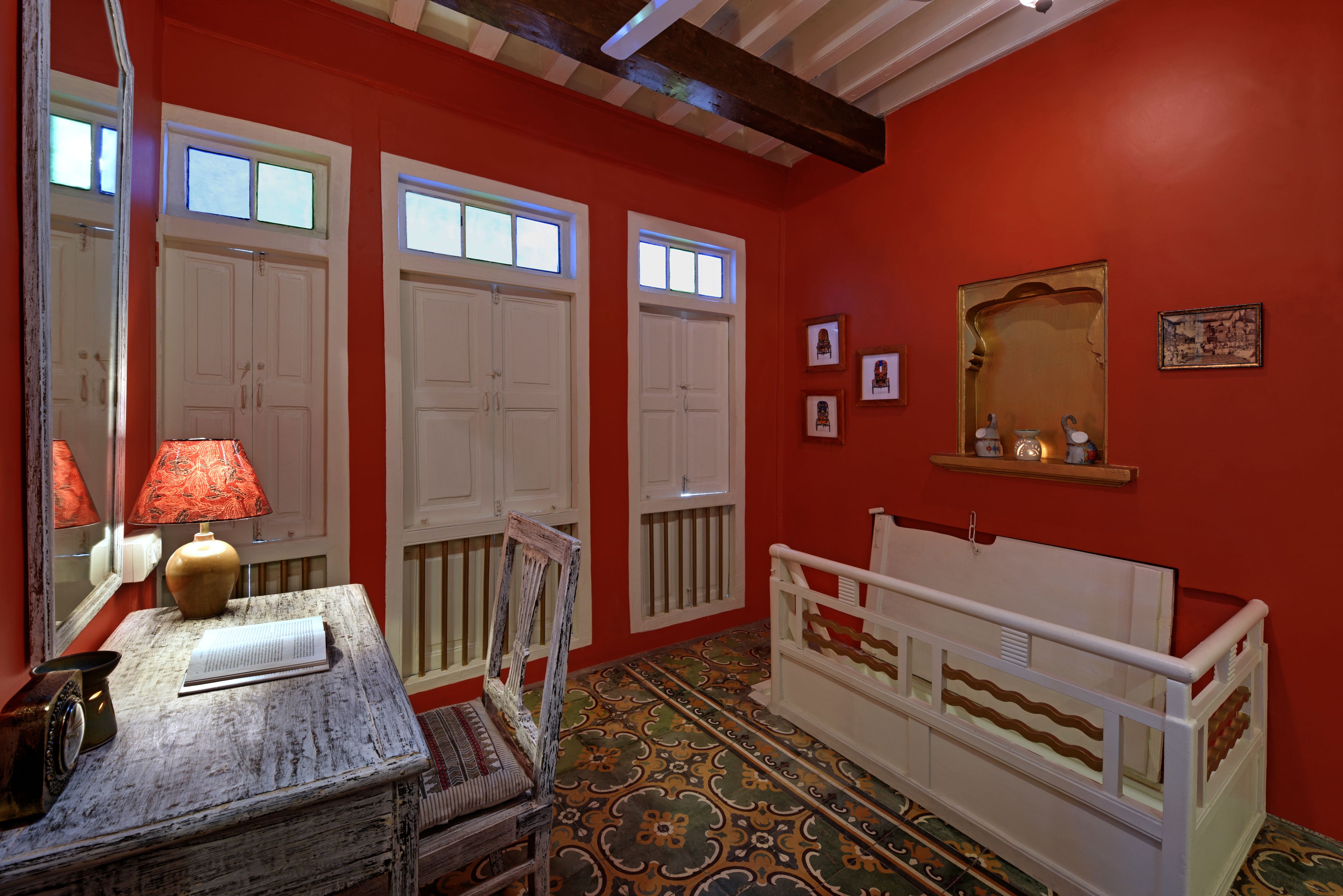 A room with red walls, white doors, a patterned floor, a small table with a lamp, and a white crib.