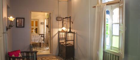 A bedroom with a bed, a wooden chair, a nightstand, a lamp, and a window with curtains.