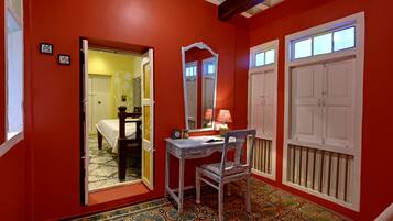 A room with a red wall, a wooden desk, a chair, a mirror, and a door leading to another room.
