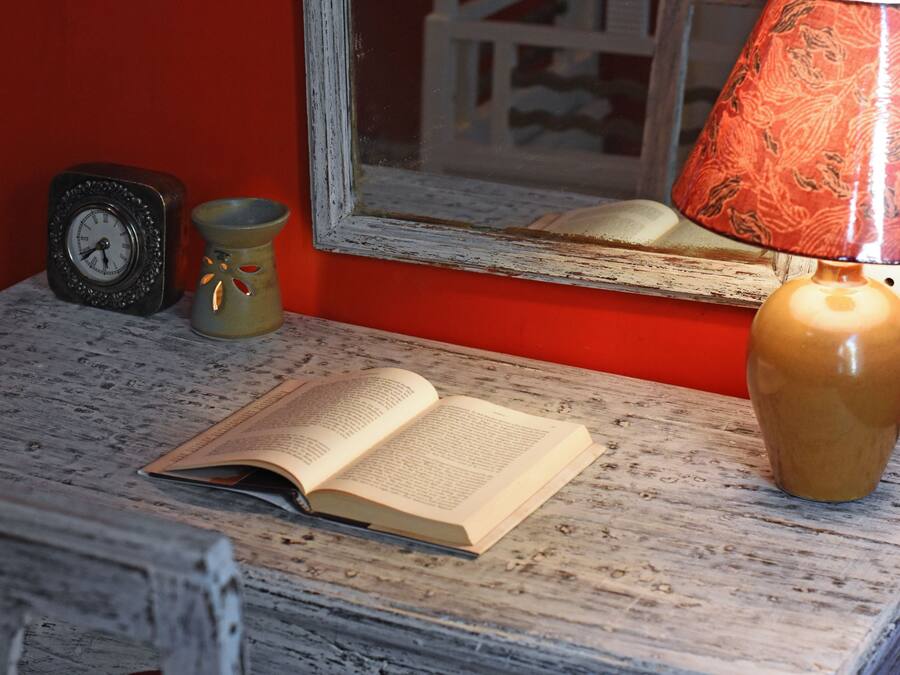 Een houten tafel met een open boek, een klok, een vaas en een lamp.