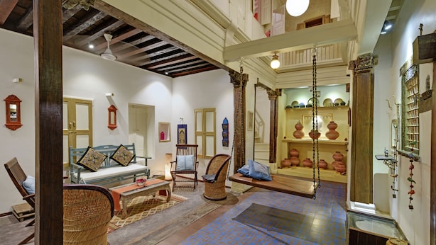 A traditional interior with a wooden ceiling, a patterned floor, and a collection of pottery and decorative items on shelves. - French Haveli (Ahmedabad)