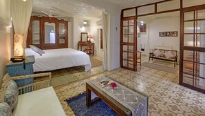 A bedroom with a bed, a bedside table, a lamp, a mirror, and a wardrobe. - French Haveli (Ahmedabad)