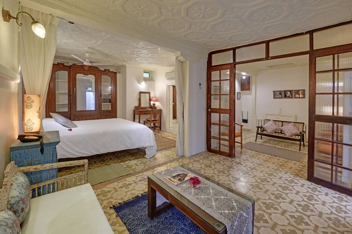 A bedroom with a bed, a bedside table, a lamp, a mirror, and a wardrobe.