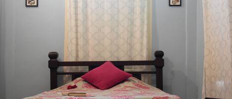 A bed with a patterned bedspread, a single red pillow, and a book on the bed.