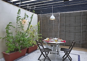 A patio with a table set for breakfast, surrounded by potted plants and a pergola.