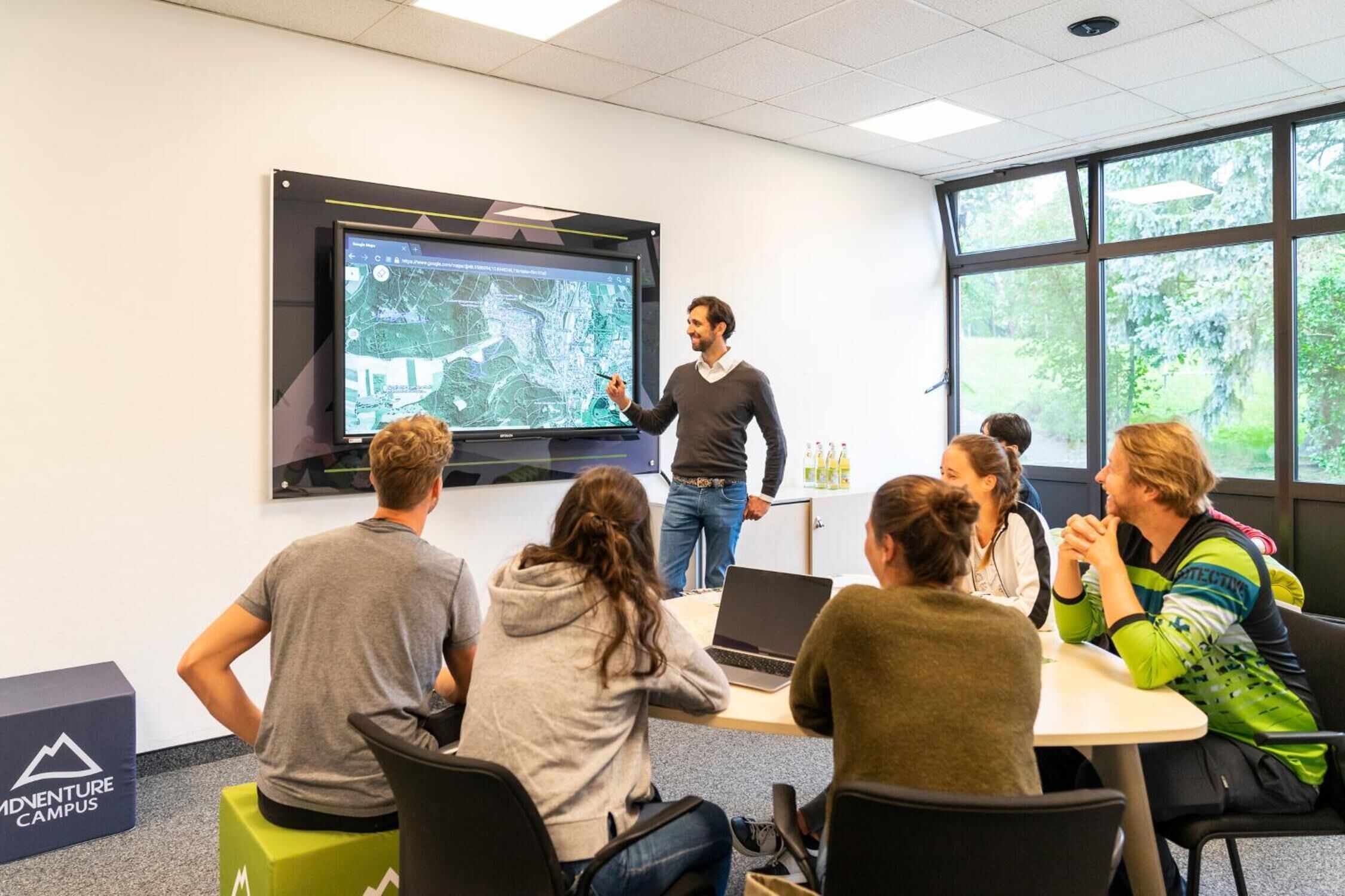 A presentation in a room with a large screen, a projector, and a group of people seated around a table.