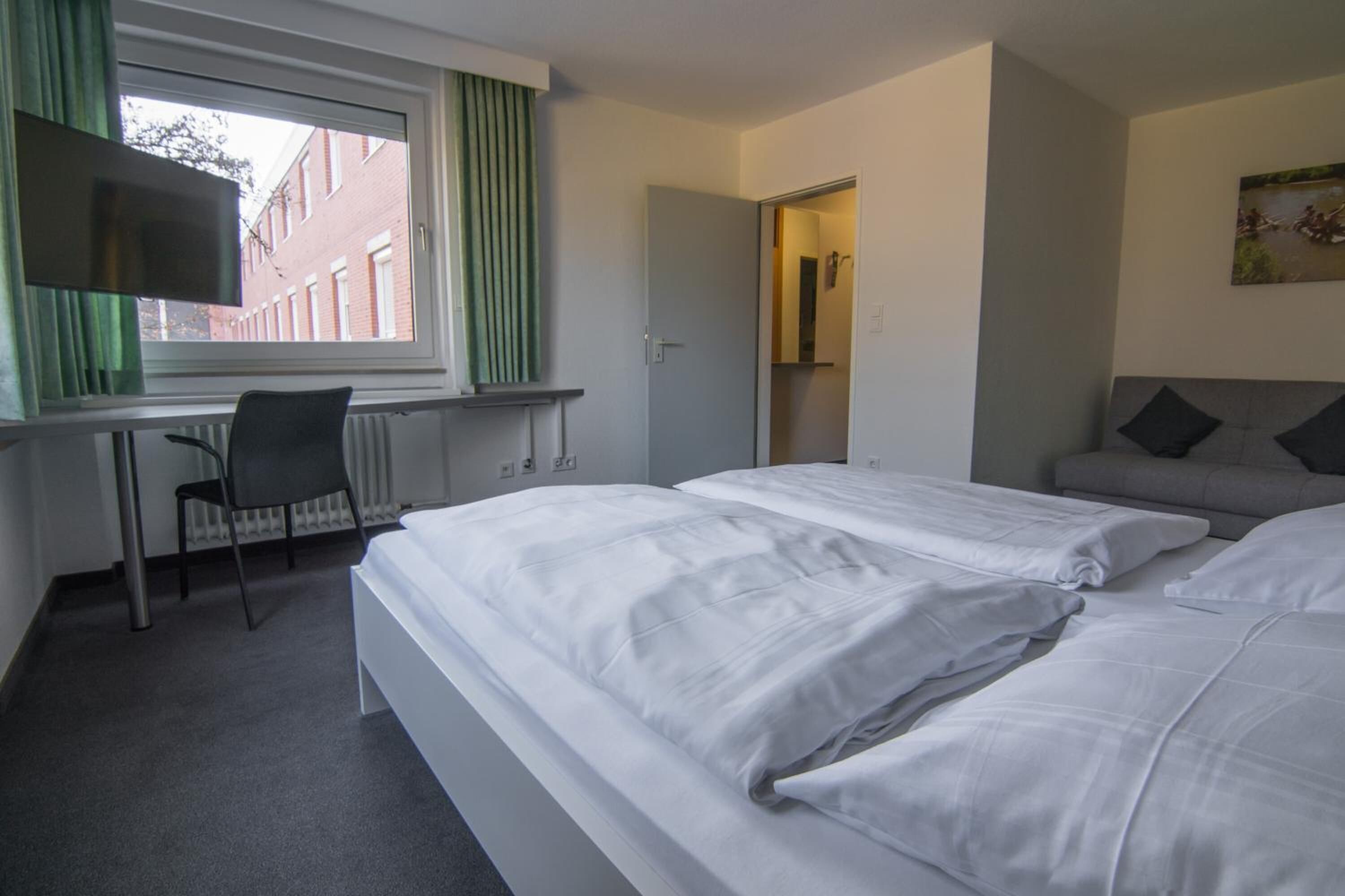 A hotel room with two beds, a desk with a chair, a TV, and a window with curtains.
