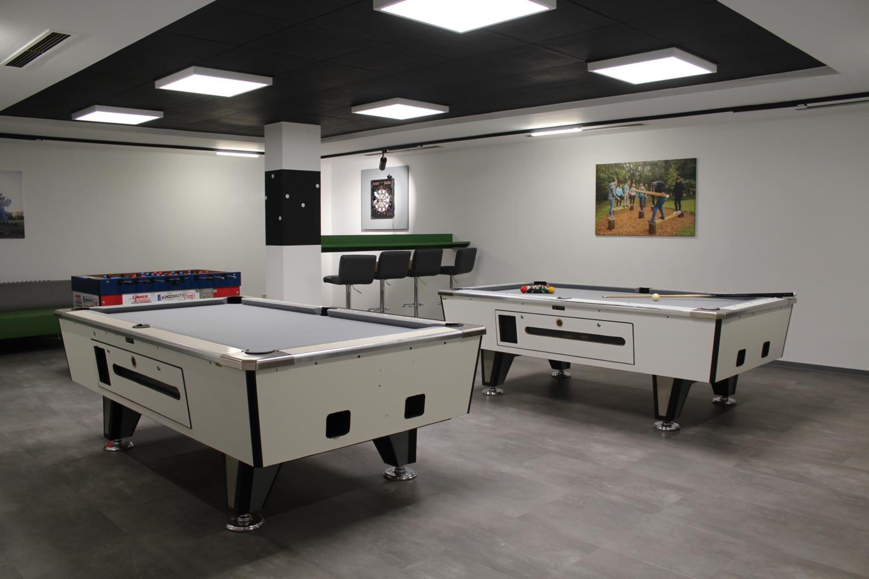 A billiards room with two pool tables, chairs, and a green cabinet.