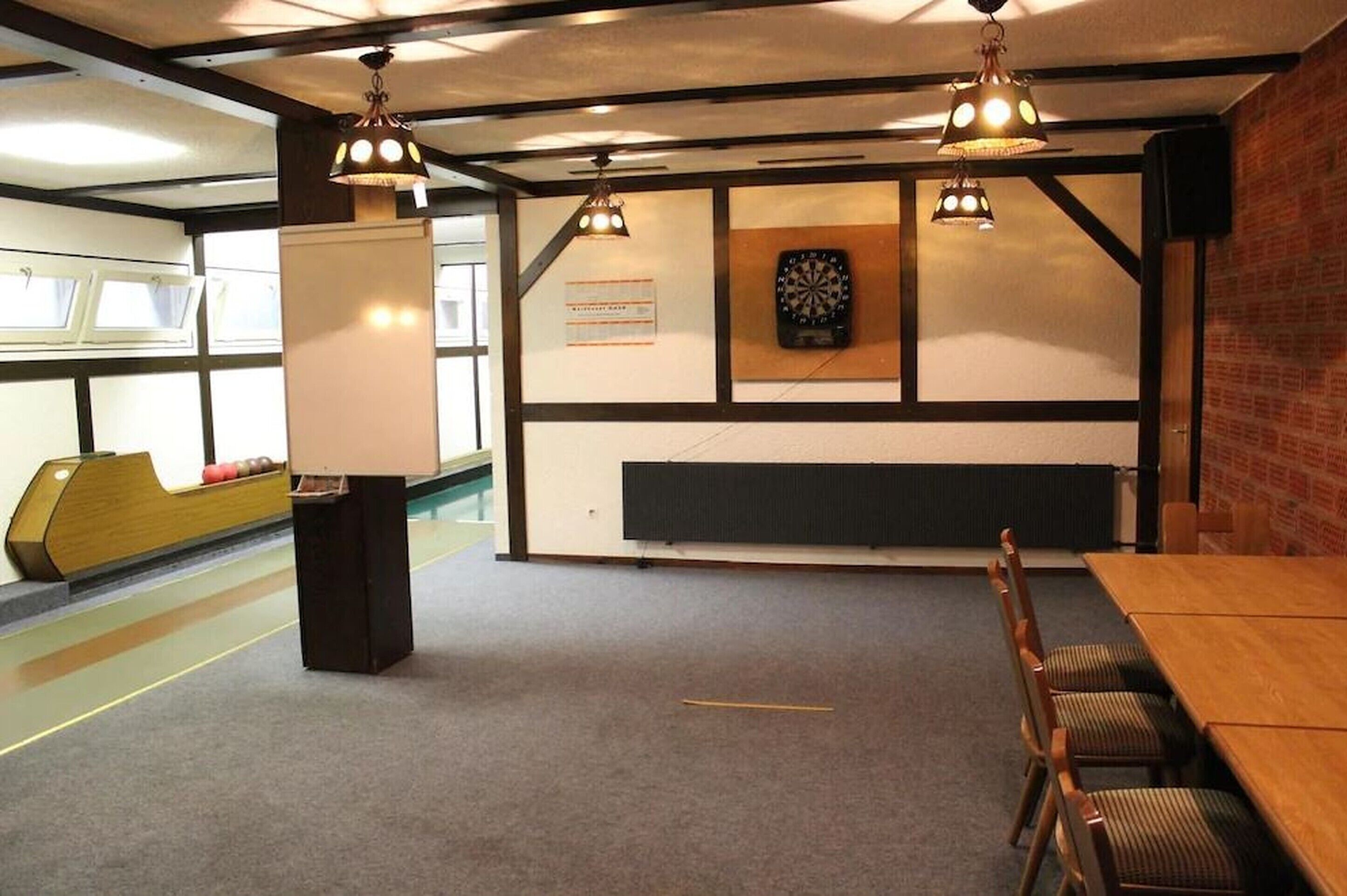 A bowling alley with a wooden table and chairs, a dartboard, and a whiteboard.