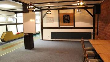 A bowling alley with a wooden table and chairs, a dartboard, and a whiteboard.