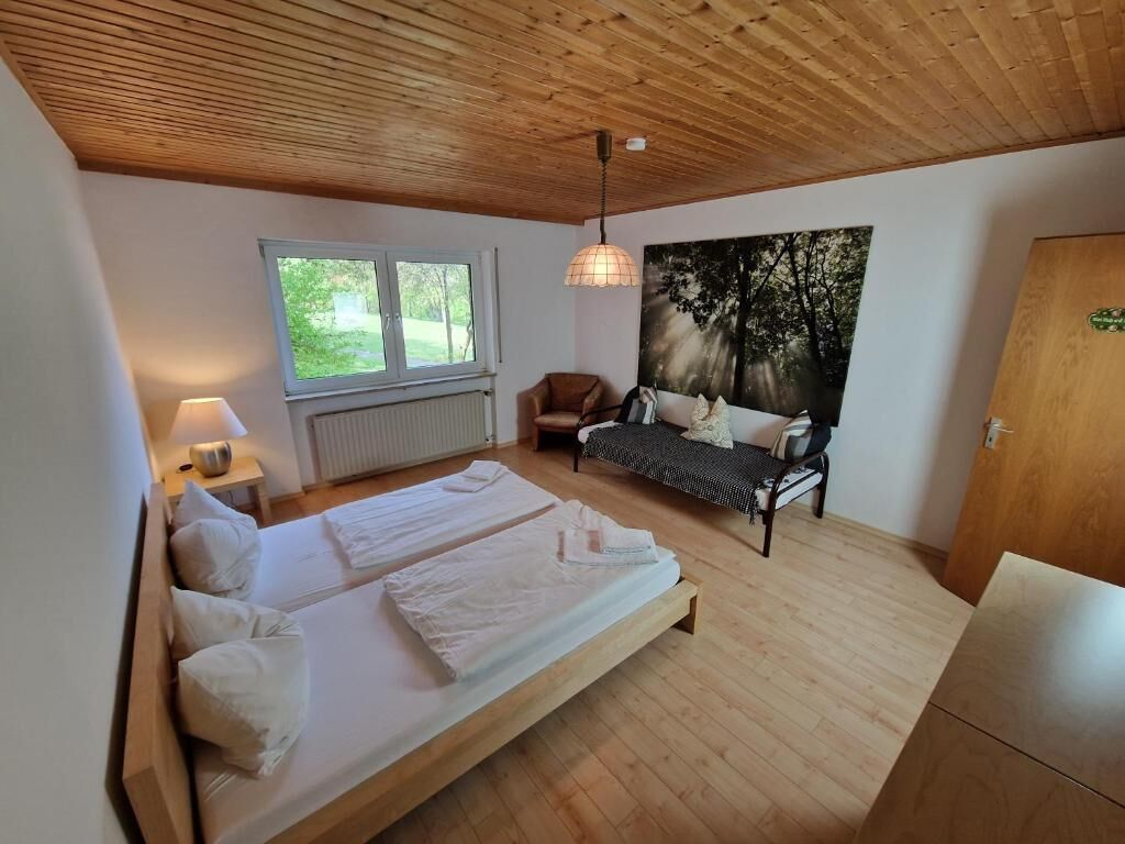 A bedroom with a large bed, a window, a sofa, and a painting.