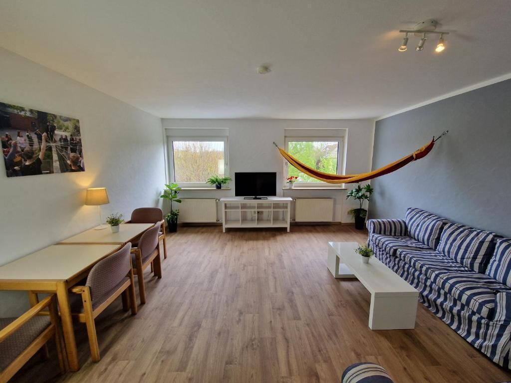 A living room with a sofa, a dining table with chairs, a TV, and a hammock.