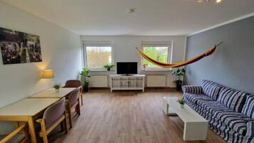 A living room with a sofa, a dining table with chairs, a TV, and a hammock.