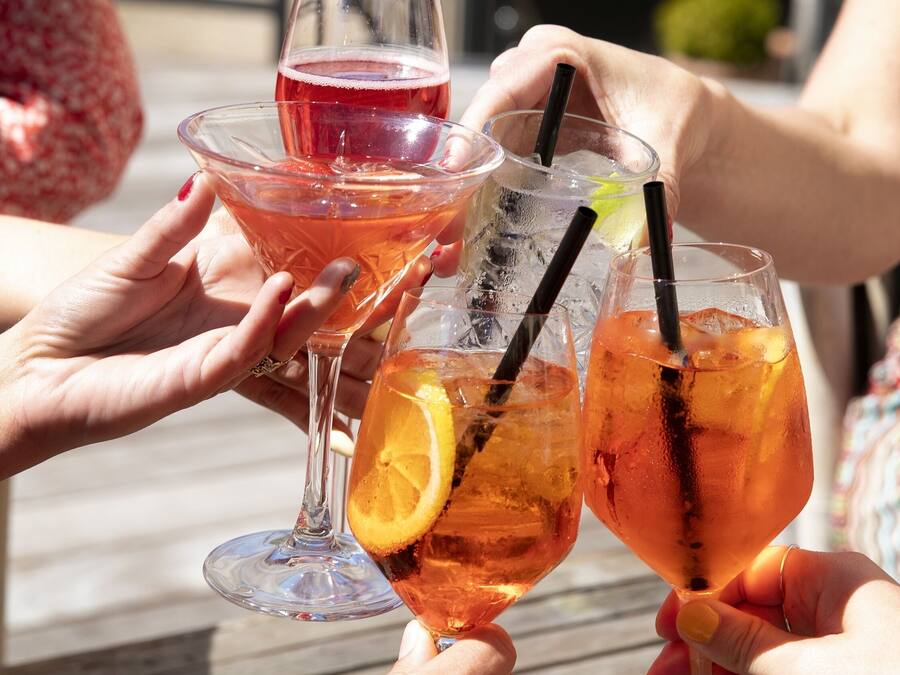 Een groep mensen proost met drankjes aan een buitentafel.