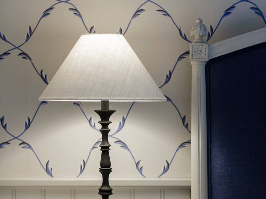 Una mesita de noche con una lámpara, una mesita auxiliar y una pared con un diseño de hojas azules.