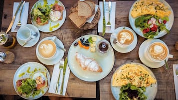 Una mesa de madera dispuesta con diversos platos de desayuno, incluyendo huevos, tostadas y pasteles, junto con tazas de café.