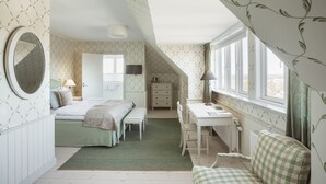 A bedroom with a bed, desk, chair, and a window with curtains.
