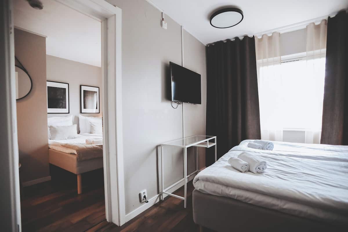 A hotel room with a bed, a TV mounted on the wall, a bedside table, and a window with curtains.