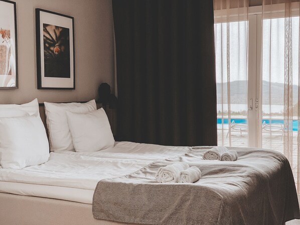 A hotel room with a bed, white pillows, a dark curtain, and a view of a pool through a large window. - Siljansnäs Hotell (Siljansnas)