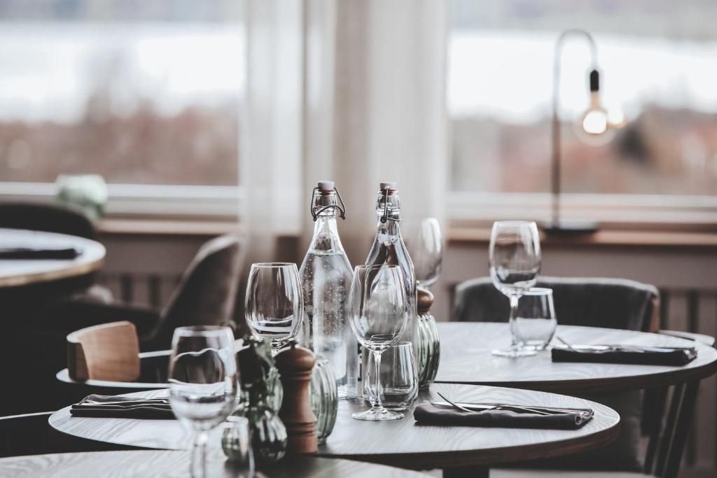 Mesa de comedor dispuesta con copas de vino, botellas y cubiertos, con vistas al exterior a través de una ventana.