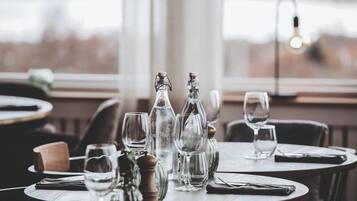Mesa de comedor dispuesta con copas de vino, botellas y cubiertos, con vistas al exterior a través de una ventana.