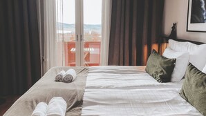 Habitación de hotel con una cama, dos toallas enrolladas, vistas a través de una puerta de cristal y un cuadro colgado en la pared.