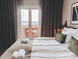 Habitación de hotel con una cama, dos toallas enrolladas, vistas a través de una puerta de cristal y un cuadro colgado en la pared.
