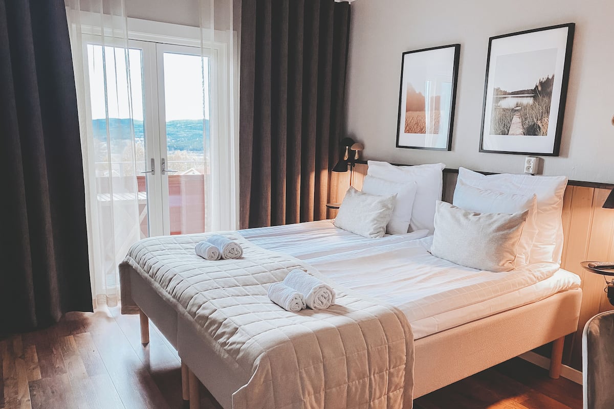 A hotel room with a large bed, a view through a glass door, and two framed pictures on the wall.