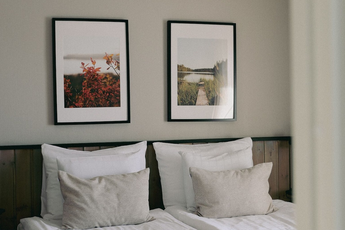 A hotel room with a bed, two framed pictures on the wall, and a wooden headboard.