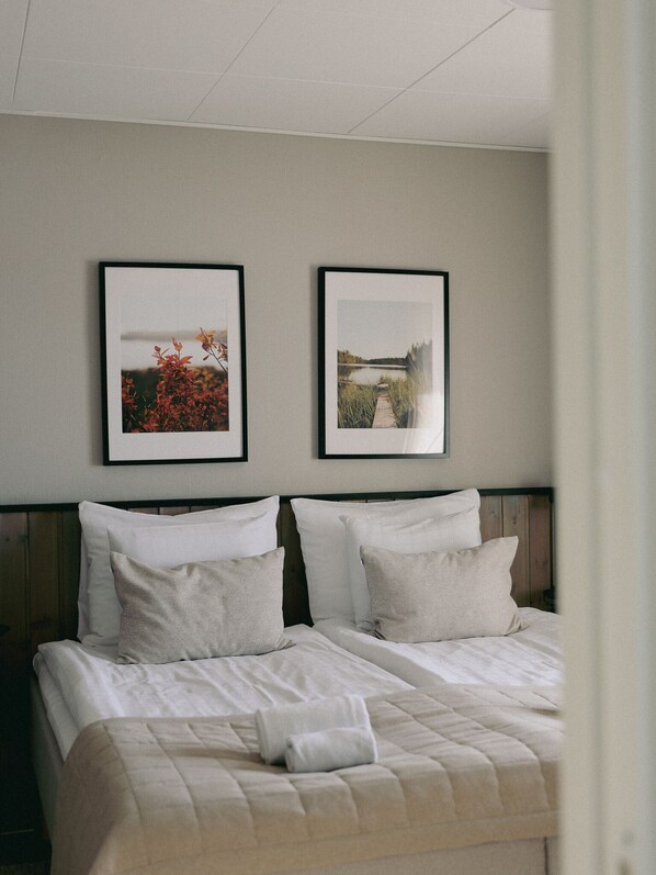 A hotel room with a bed, two framed pictures on the wall, and a wooden headboard.