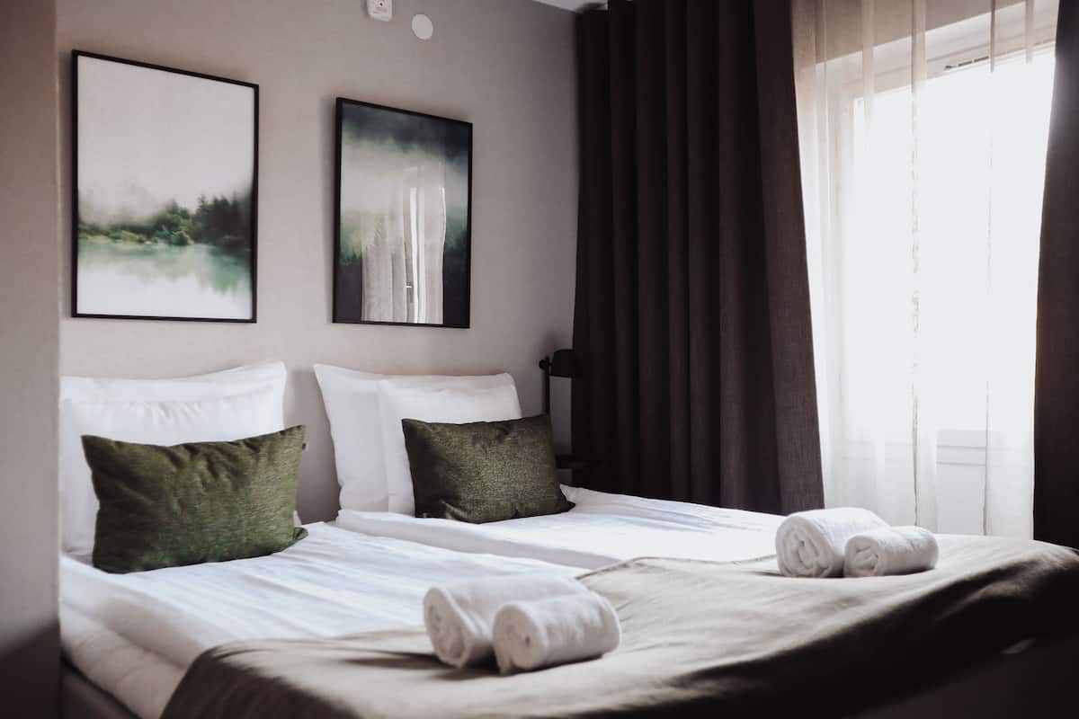A hotel room with two beds, a large window with curtains, and two framed pictures on the wall.