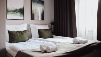 Una habitación de hotel con dos camas, un ventanal con cortinas y dos cuadros en la pared.