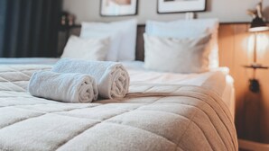 Una cama bien hecha con toallas blancas enrolladas, un edredón acolchado y un cabecero con dos cuadros en la pared.