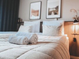 Una cama bien hecha con toallas blancas enrolladas, un edredón acolchado y un cabecero con dos cuadros en la pared.