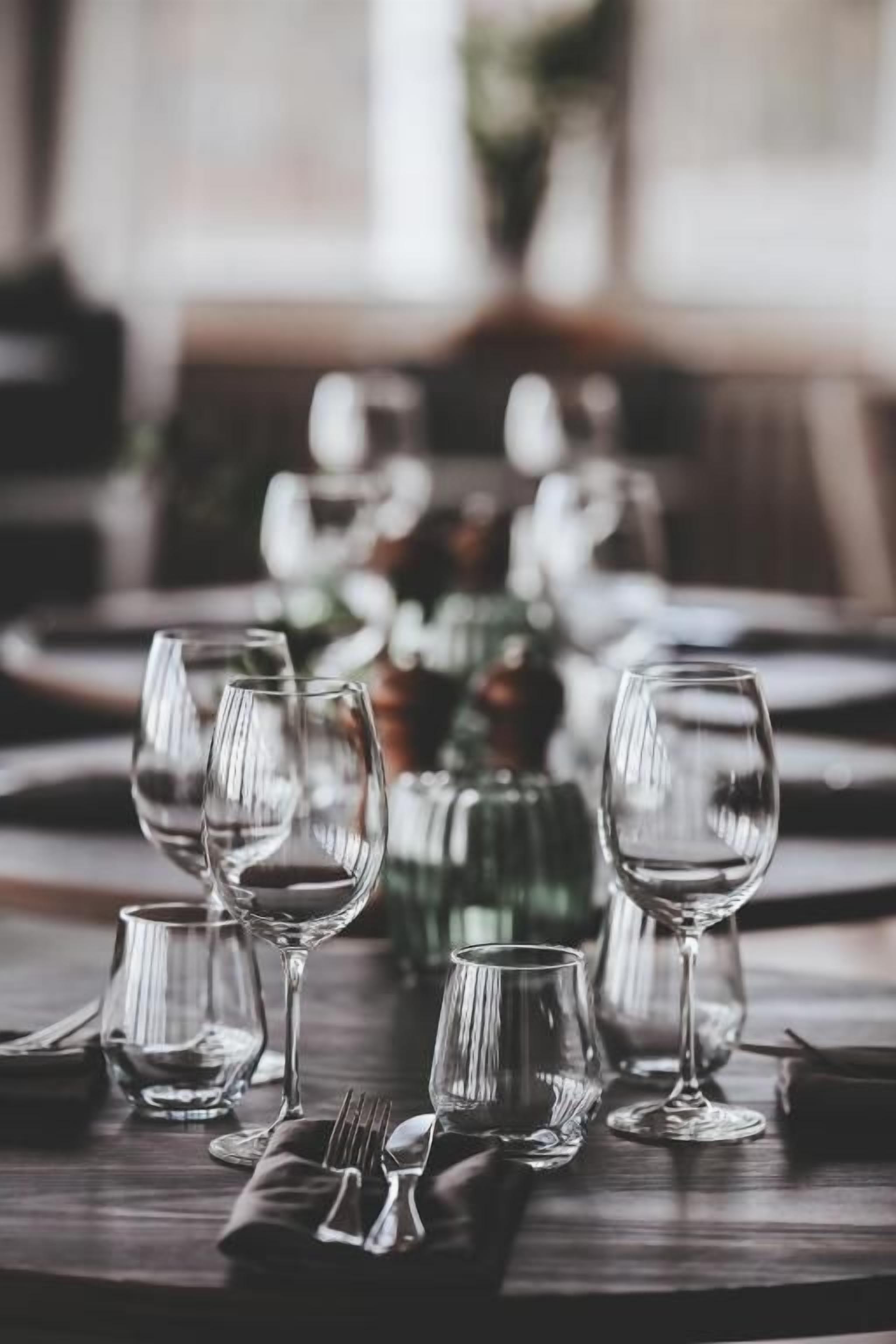 Une table à manger dressée avec plusieurs verres à vin, des couverts et une bouteille verte, vraisemblablement une bouteille de vin.