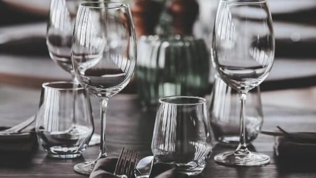 A dining table set with multiple wine glasses, cutlery, and a green bottle, likely a wine bottle. - Siljansnäs Hotell (Siljansnas)