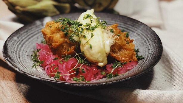 Un plato de comida con un huevo escalfado, adornado con microgreens, acompañado de vegetales encurtidos.