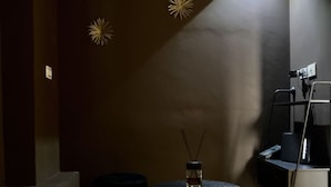 Une pièce faiblement éclairée, avec une table ronde, deux poufs noirs et un petit vase contenant des bâtonnets d’encens.