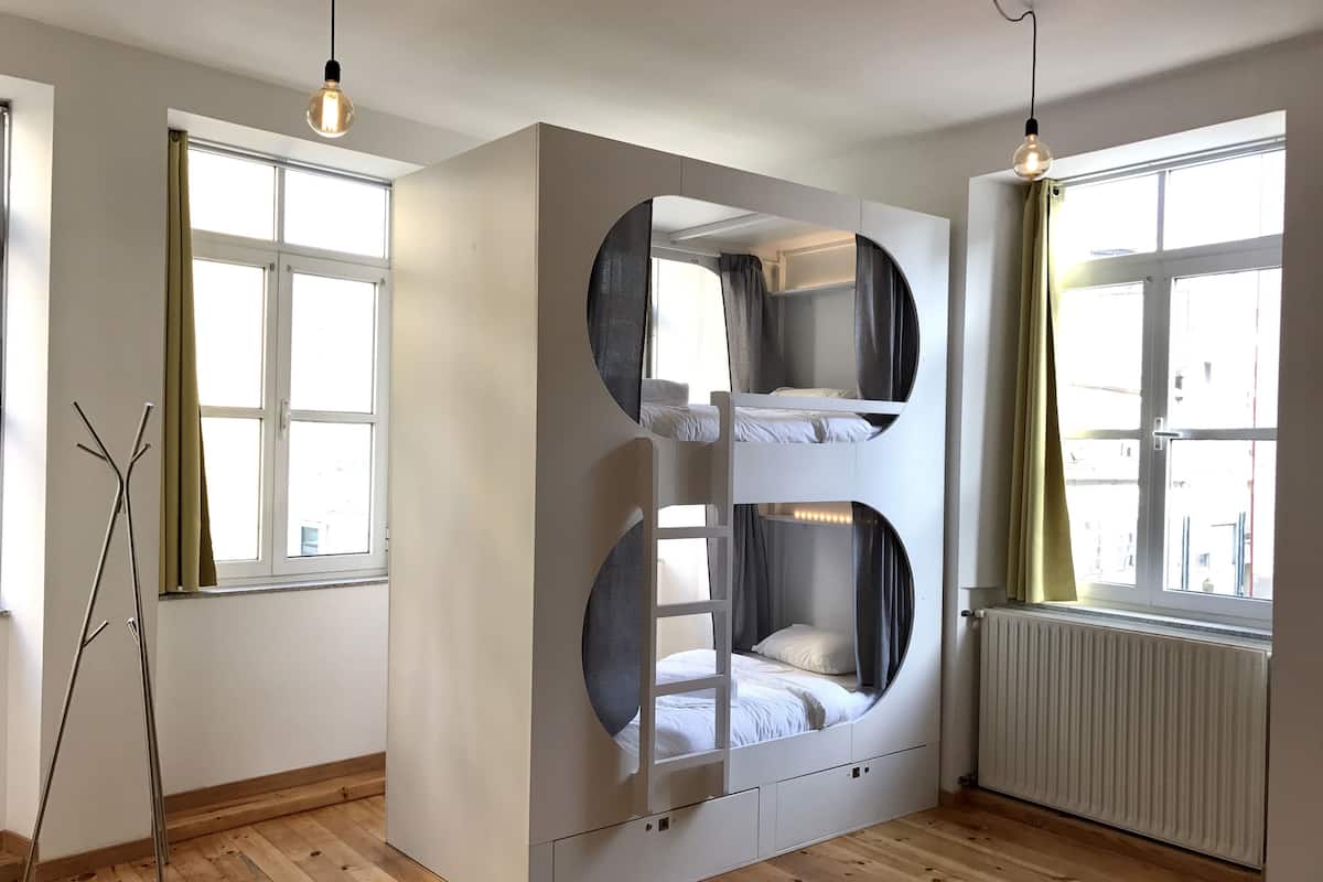 A room with a bunk bed, a radiator, and a window with curtains.
