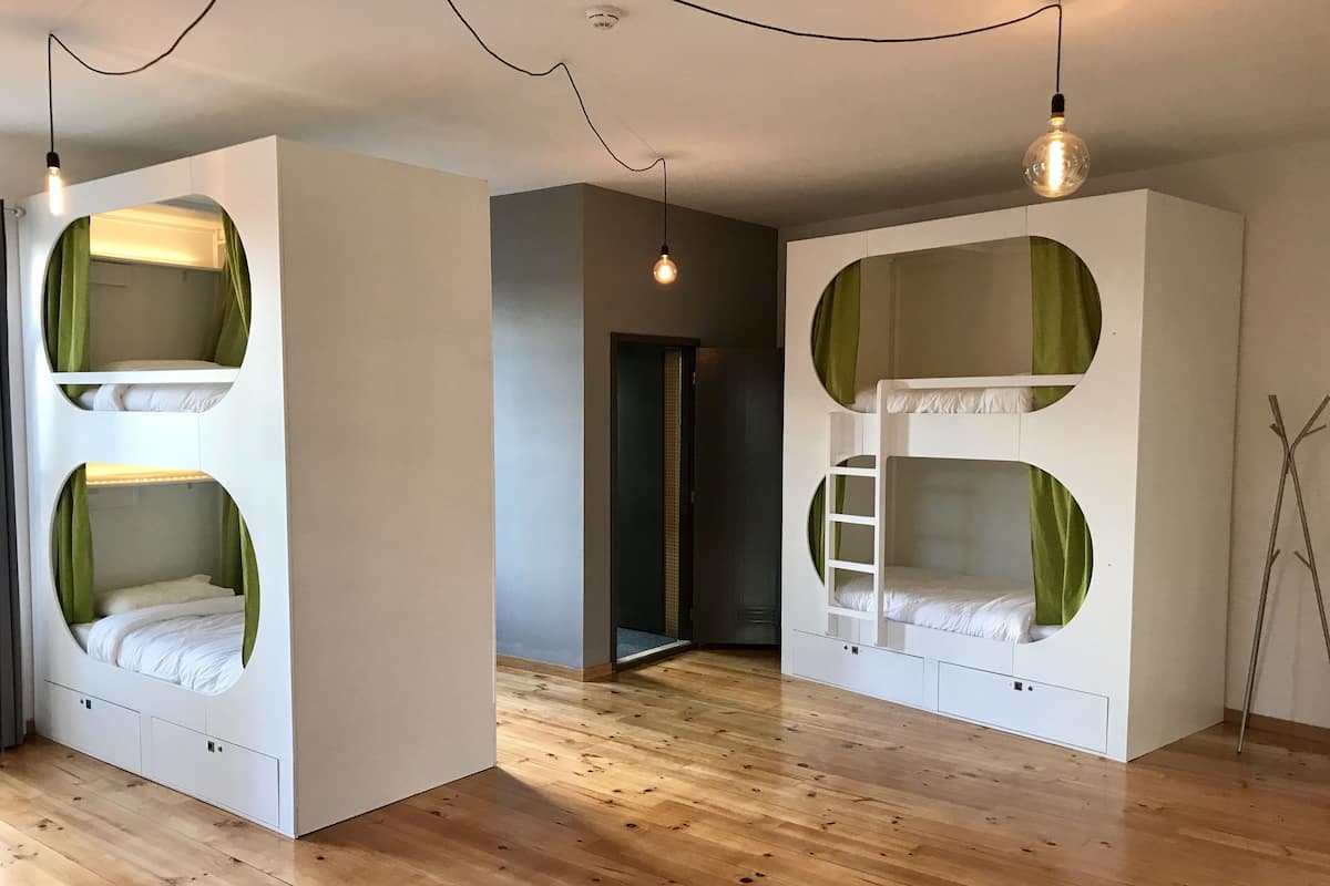 A room with bunk beds, wooden flooring, and a light bulb hanging from the ceiling.