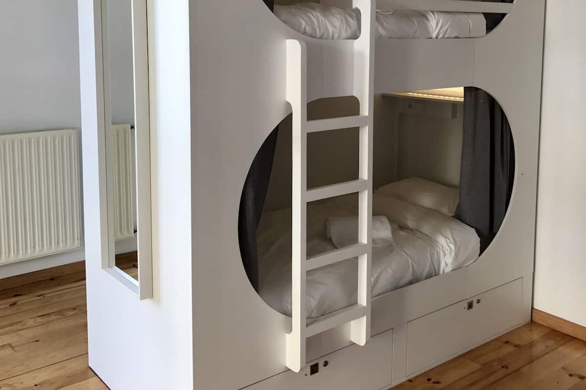 A bunk bed with a ladder, a mirror, and a white wardrobe in a room with wooden flooring.