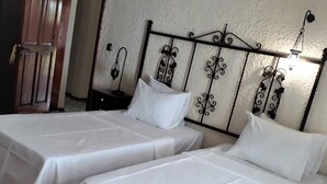 A room with two single beds, each with a white bedspread and pillow, against a textured wall with a decorative metal headboard. - Zeydali Hotel (Gökçeada)